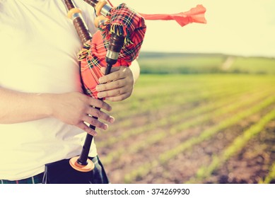 Close Up View Of Man Enjoying Playing Pipes In Scotish Traditional Kilt On Green Field Background Outdoors 