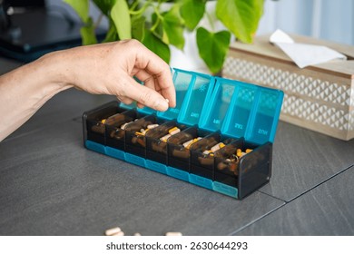 Close up view of Man hand sorting his pills and supplements into a weekly pill organizer. Concept of medication management and daily health routine. High quality photo