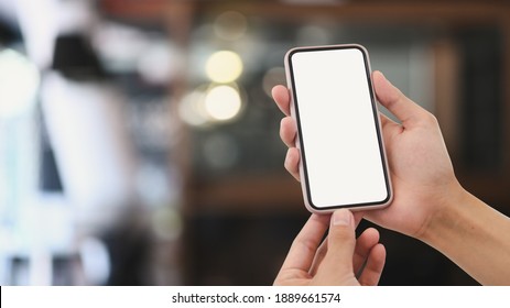 Close Up View Of Man Hands Holding Mock Up Smart Phone With Modern Cafe Blurred Background.