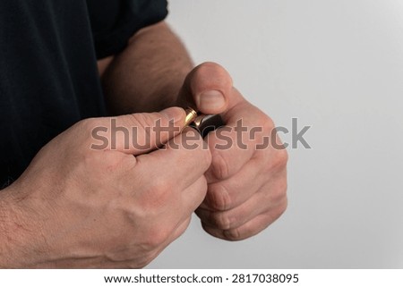 Close up view of man hands loading brass non lethal cartridge with black rubber bullet into handgun magazine on plain background.