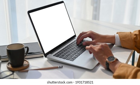 Close up view of man hands typing on keyboard of laptop computer on white desk at his home office.