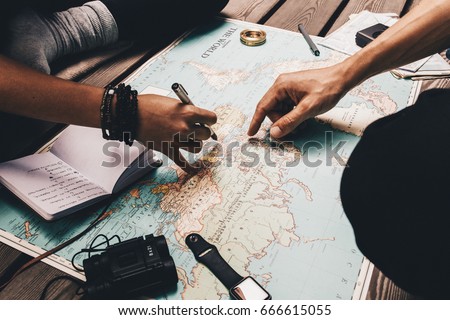 Close up view of man and woman pointing at places on world map. Woman noting vacation plan in a diary.