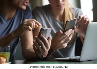 Close up view of man and woman using smartphones discussing mobile apps concept, couple talking holding cellphones synchronizing information online with laptop, checking news or texting messages