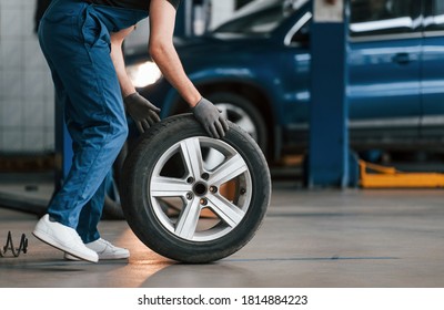Close up view of man in work uniform with car wheel indoors. Conception of automobile service.