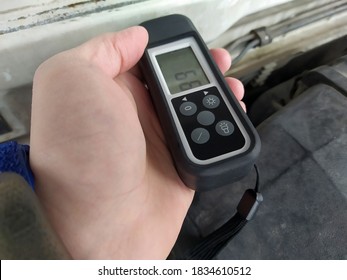 Close View Of Man's Hand Testing The Thickness Of The Car Paint In Engine Compartment. Special Device For Measurement Inspection Of Hidden Damages In Bodywork Service. Car Surface Diagnostic Tool.