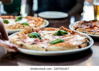 Close up view of a Margherita Neapolitan style pizza with buffalo mozzarella, tomato sauce and basil - Waiter hand serving pizza at pizza restaurant - Powered by Shutterstock