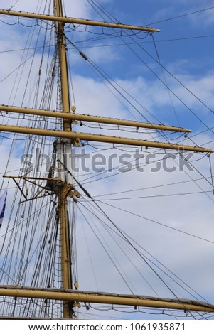 Close up view of masts and ropes of an ancient vessel with a blue cloudy sky in background. Abstract top boat image with horizontal and vertical lines. Vintage design of part of an old wooden ship.