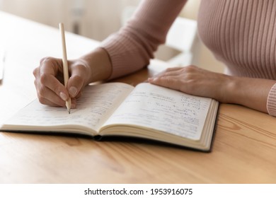 Close up view of millennial woman sit at table hold pencil take notes to paper notebook working studying. Female student businesswoman employee write records to daily planner by hand at home work desk