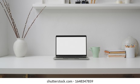 Close up view of minimal workplace with blank screen laptop, books, decorations and copy space on white desk with shelf on white wall   - Powered by Shutterstock