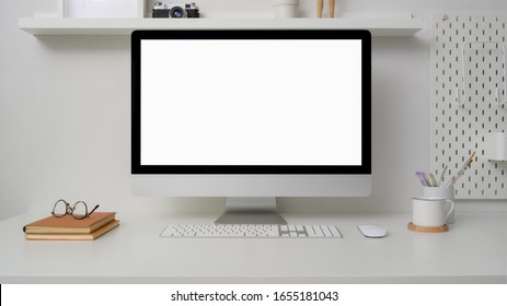 Close Up View Of Minimal Workspace With Blank Screen Computer, Office Supplies And Decorations On White Desk With Shelf On White Wall 