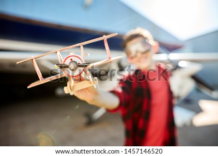 close up view of model propeller plane, blurred shot of little boy playing with the toy near hangar building. Aircrafts and aeromodelling hobby concept.