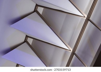Close up view of a modern ceiling with architectural triangular panels and linear metal framing, illuminated by ambient purple light