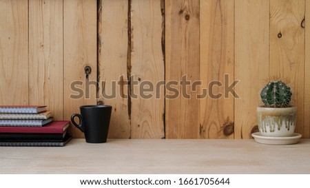 Close up view of modern rustic workspace with mug, notebooks, cactus pot and copy space on wooden desk with wooden plank wall