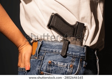 Close up view of a modern semi automatic handgun pistol inside an IWB waistband holster on a woman wearing casual denim jeans.