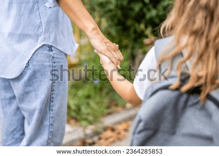 Close up view of mother and daughter holding hands together as walking towards the school.