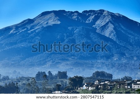 Close view of Mount Merbabu slopes with morning mist, village houses, and agricultural fields in Central Java, Indonesia