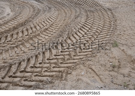 Close up view of muddy ground with multiple tractor tire marks forming repeating lines and curves