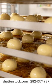 close view of multiple glazed dough balls resting on metal bakery racks during proofing, with shiny egg wash, shallow depth of field, warm light, and tidy rows dough