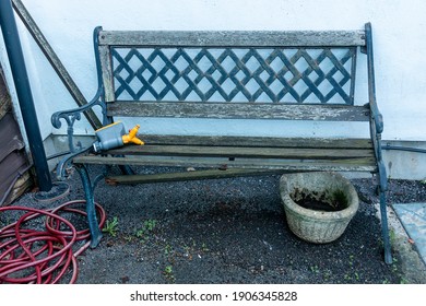 A Close Up View Of A Old Broken Metal And Wood Garden Chair With A Hose Pipe And Old Pot Plant Next To It 