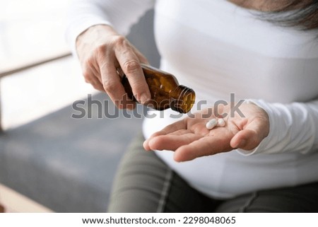 Close up view of old lady taking out the pills from the bottle while sitting on the sofa.