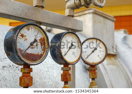 Close up view of old rusty damaged metal meter, valve tube system and gas or liquid tank for industry. Detail of broken circular measurement meter with rusty dial.