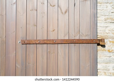 Close up view of an old wooden door  made from vertical planks and attached to limestone wall. Boards are covered with transparent preservative that emphasizes timber texture. Old rusted iron hinges.