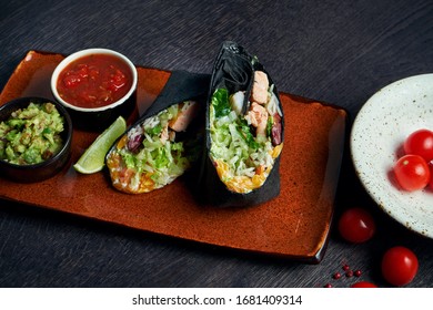 Close Up View On Burrito With Salmon, Lettuce, Rice, Tomatoes, Corn And Bell Pepper In Black Pita On A Brown Plate With Tomato Salsa And Guacamole. Vegetarian Shawarma Roll