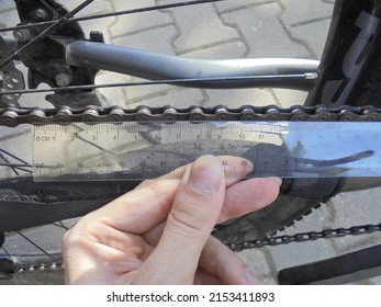 Close view on manual checking of bike chain wear and tear degree by measuring the length of segments with a transparent plastic ruler.