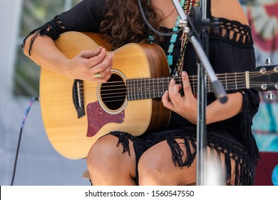 a close up view on musician woman playing the guitar, hands of female guitarist on outdoor stage during a live music gig in nature