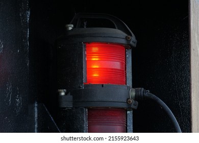 Close View On Red Port Side Navigational Lights Of The Container Ship. Bulb Is Inside The Oval Black Plastic Cover With Red Plexiglass. Whole Lamp Is Inside Black Metal Box.