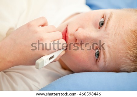 Close up view on sick boy using white digital thermometer while laying down on blue linen pillow