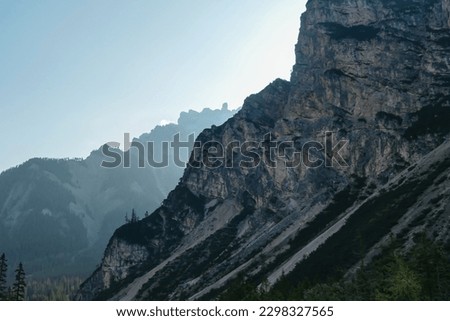 A close up view on a steep mountain wall in Italian Dolomites. There is another mountain chain behind it. The sunbeams reaching back sides of the mountain. The slopes are stony and sharp. High Alps.