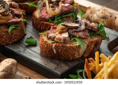 Close Up View Of An Open Faced Steak Sandwich Topped With Sauteed Mushrooms And Onions And Arugula.