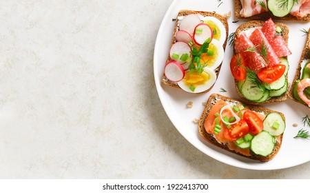 Close up view of open sandwiches with meat, vegetables, seafood on plare over light stone background with free text space. Top view, flat lay.