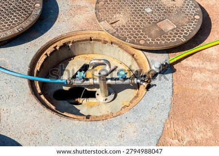 Close view of an open utility pit with metal valve assembly and connected hoses prepared for temporary water and service distribution at a caravan support area.
