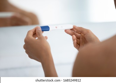 Close up view over shoulder of woman hold positive pregnancy quick plastic test with two red stripes confirm that female is pregnant. New life, feminine health, happy changes and fertilization concept
