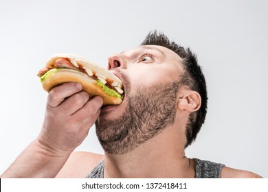 close up view of overweight man in tank top eating hot dog isolated on white