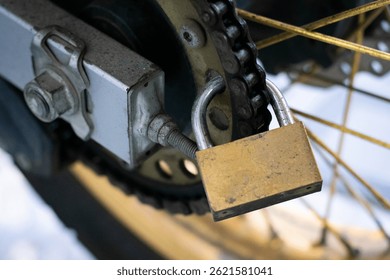 close up view of a padlock installed on a motorcycle chain as an additional anti-theft security system.
