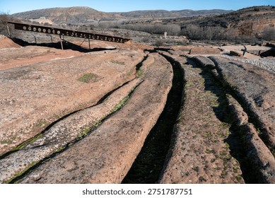 Close view of parallel grooves and channels carved into bedrock at Tiermes Archaeological Site in Soria, Castilla y León, Spain, showing ancient rock-cut infrastructure.