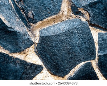 A close up view of a patterned black stone wall, showcasing the rough textures and unique shapes of the stones.