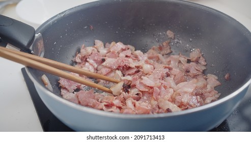 close up view of person roasted chopped crispy bacon strips slices in a Hot Skillet frying pan with hot oil splashing, rich in fat and color, sizzling and smoking, morning breakfast	
