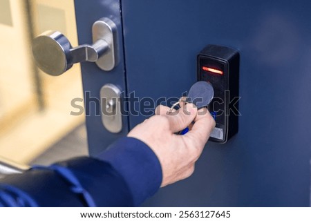 Close up view of person using a electric lock key fob to access a building via a reader of entry system mounted on a house wall. High quality photo