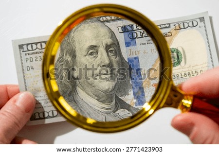 Close up view of a person using a magnifying glass to examine a one hundred dollar bill on a table