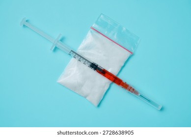 Close up view of a plastic bag containing white powder and a medical syringe on a light blue background.