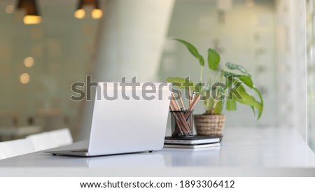 Close up view of portable workspace with laptop, stationery and plant pot o the table in co-working space