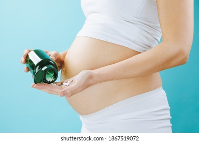 Close up view of pregnant belly and vitamin pills in the hand isolated on blue background