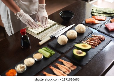 Close up view of process of preparing rolling sushi. Nori and white rice. Chef's hands touch rice. Chef starts cooking sushi