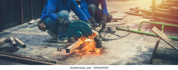 Close up view of professional focused two worker man in uniform working on the metal pipe sculpture with an electric grinder while sparks flying in the industrial outdoor site constuction. - Powered by Shutterstock