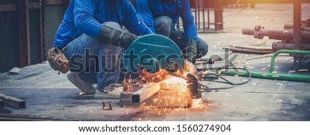 Close up view of professional focused two worker man in uniform working on the metal pipe sculpture with an electric grinder while sparks flying in the industrial outdoor site constuction.