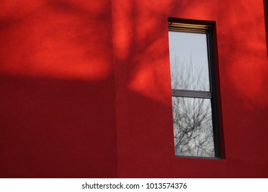 Close up view of a rectangular vertical window in a red wall. Isolated element on a painted surface. Detail of a colorful facade building and one window. Abstract urban picture. Minimalist figure.
